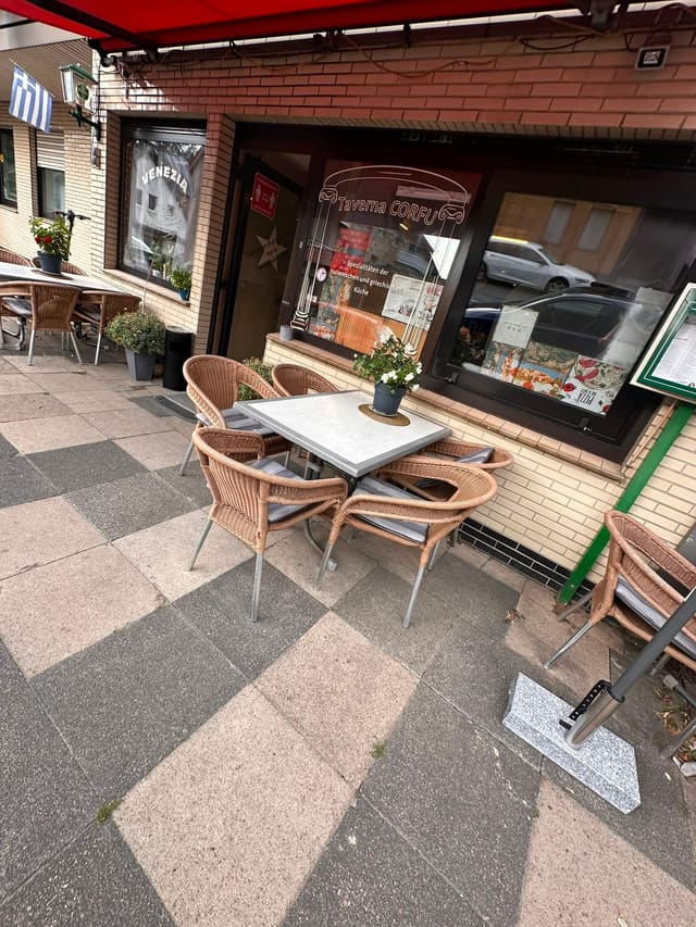 Tisch mit Korbstühlen auf der Terrasse vor dem Restaurant, unter der roten Markise
